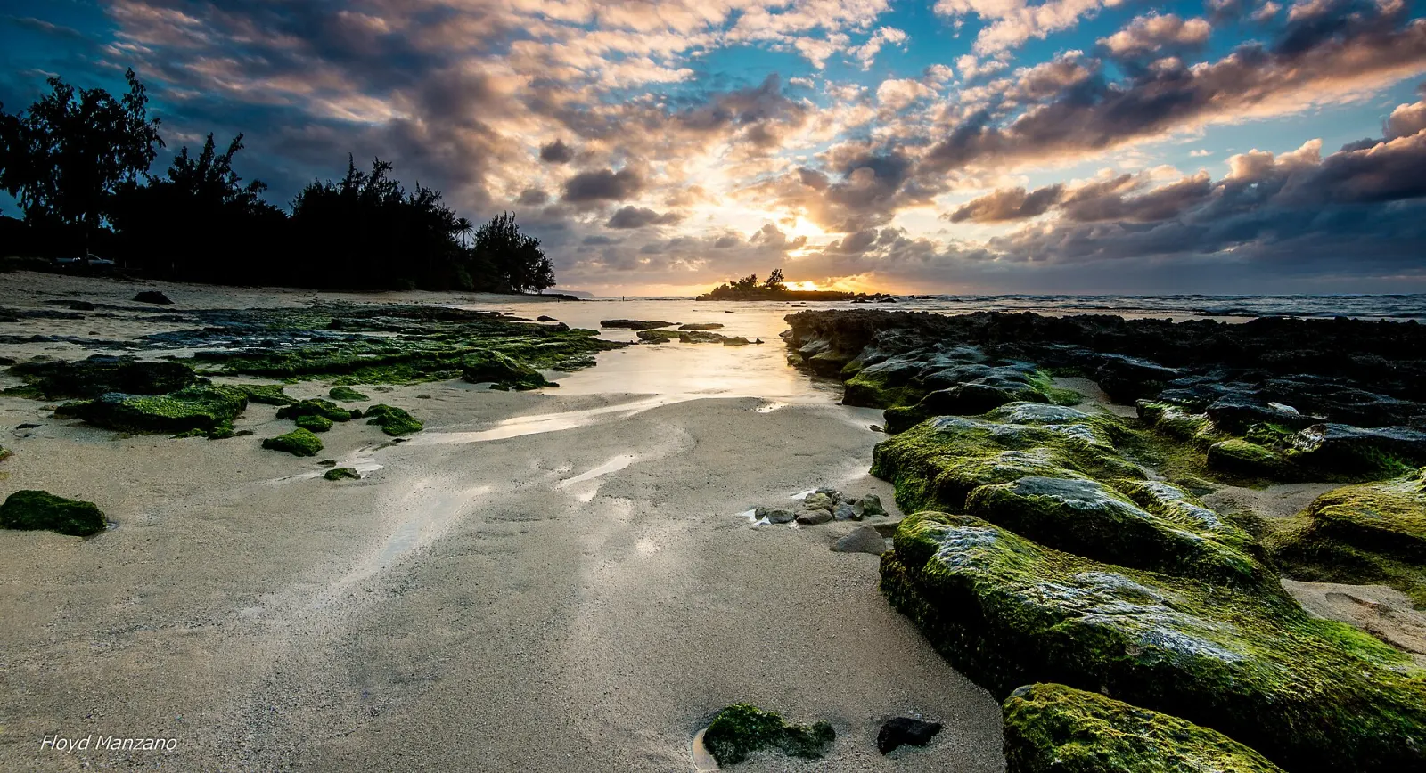 A sandy, rocky shoreline glowing at sunset at Kawela Bay Beach Park
