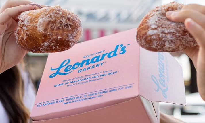 Two malasadas held above a Leonard's Bakery box